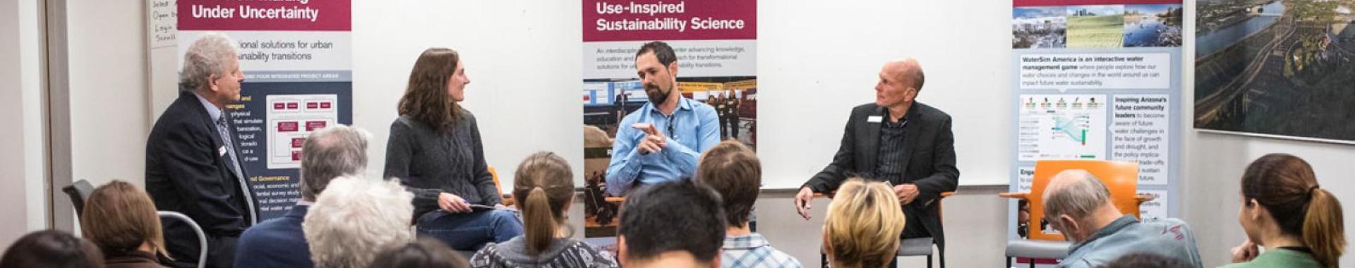 People sitting on a board panel speaking to a crowd